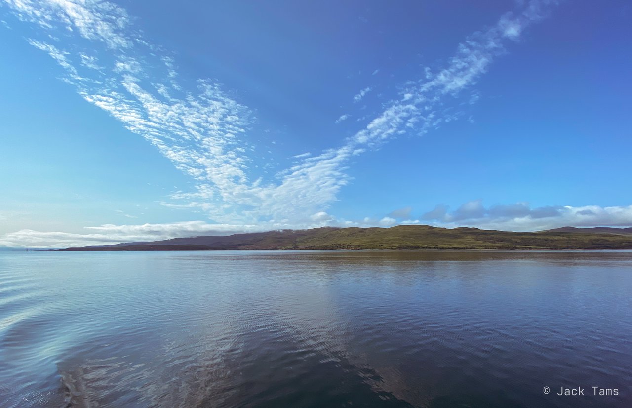 A flat calm morning on the water, an island low on the horizon.