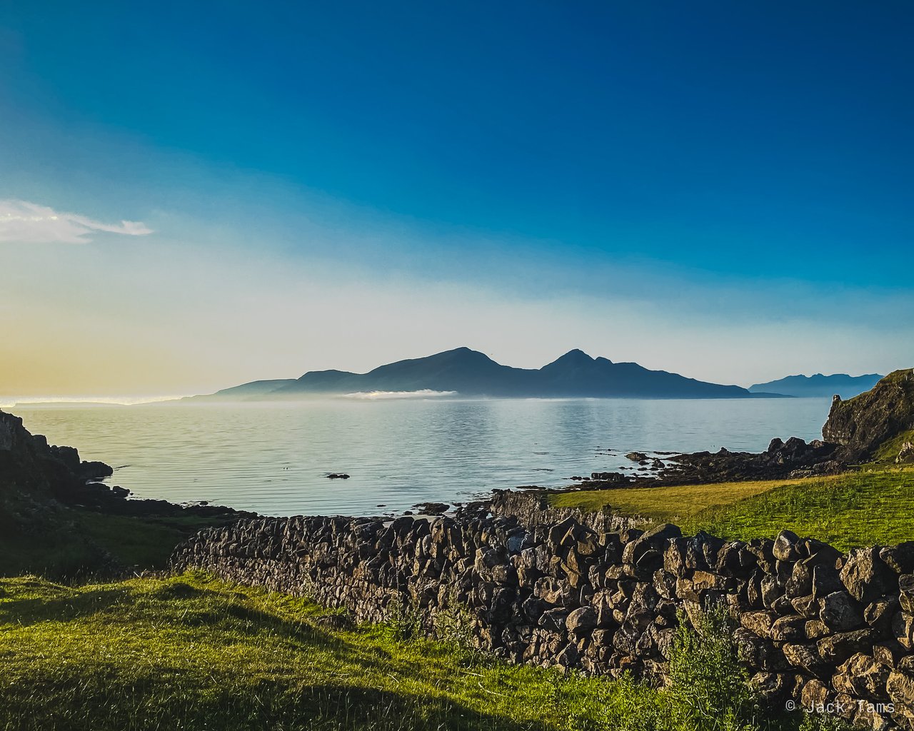 Islands across the water from the shore, a dry-stone wall in front.
