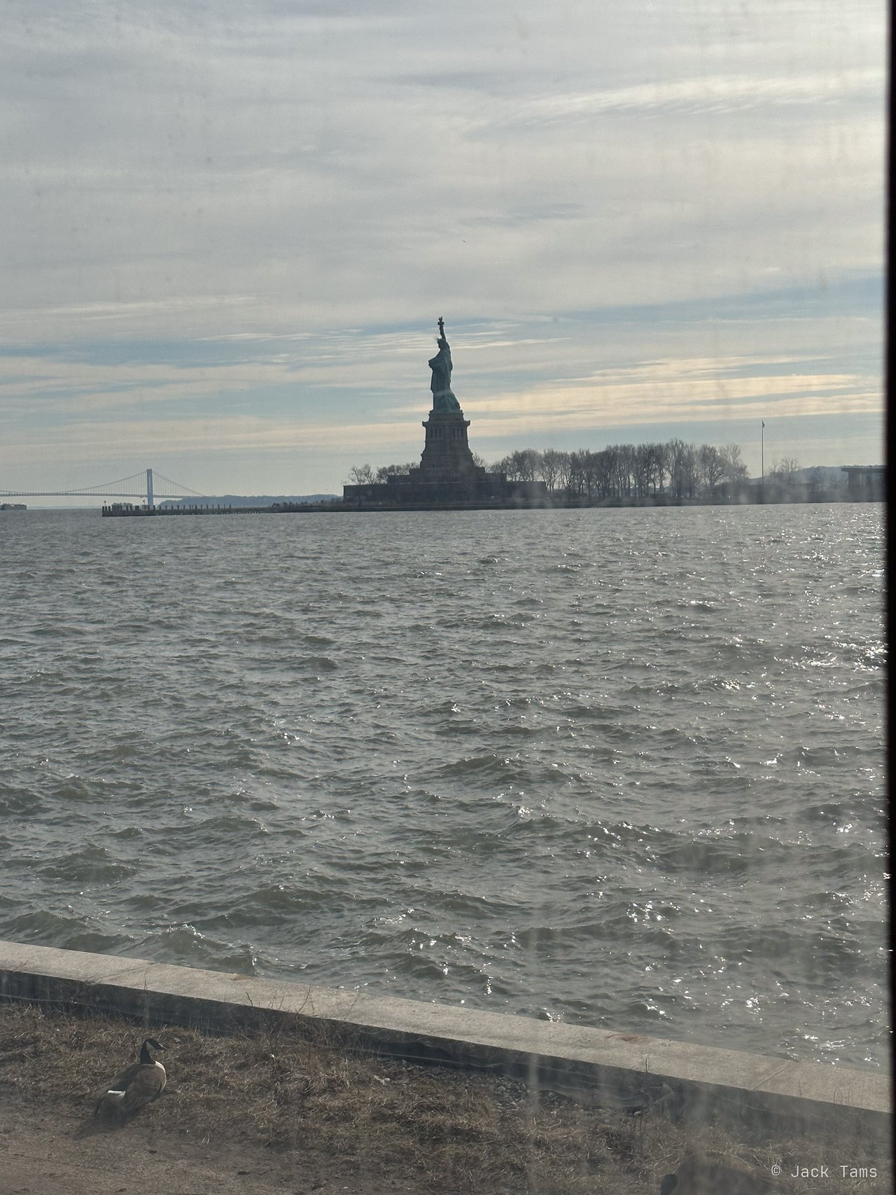 The Statue of Liberty across the grey water from Ellis Island.