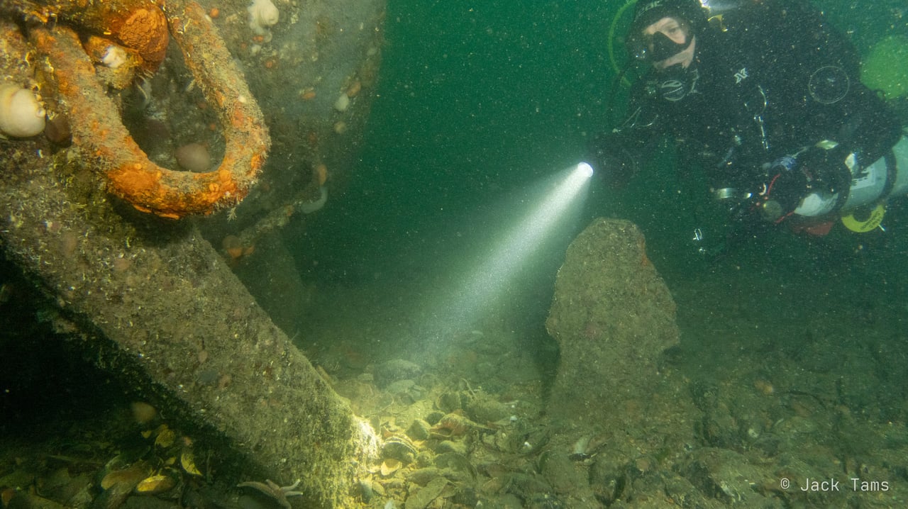 A diver with a torch beside an anchor chain on a German wreck.