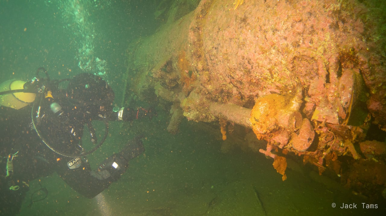 A diver with a torch along machinery on the wreck.