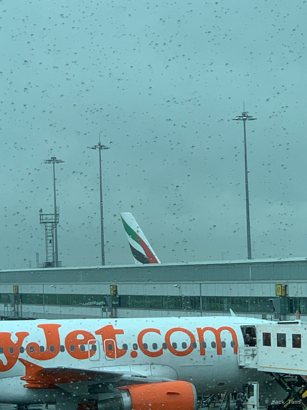An Emirates A380's tail beyond an easyJet, in the rain.