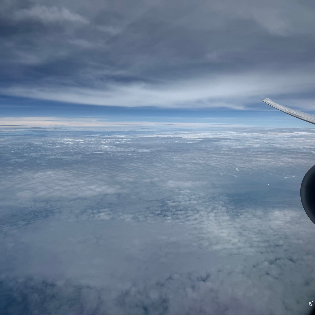 The 777's wing and engine over the cloud.